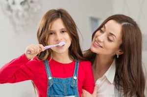 little girl practices dental hygiene with mom